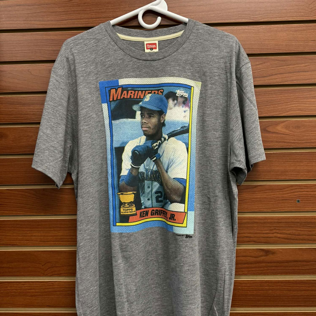 Celebrate baseball history with this iconic Topps Baseball Ken Griffey Jr 1990 Grey T-Shirt. Featuring the legendary "The Kid" in his prime, this vintage-inspired tee captures one of baseball's most memorable card designs. Perfect for collectors, nostalgia enthusiasts, and Griffey fans alike, this comfortable grey shirt lets you wear your passion for the sport. Whether you're hitting the ballpark or showing off your baseball knowledge, this timeless piece connects you to one of the greatest players ever to 